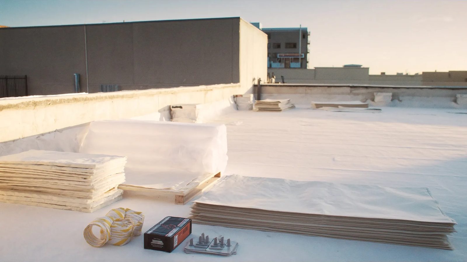 Rolls of TPO membrane and polyiso boards staged on a flat roof in morning light
